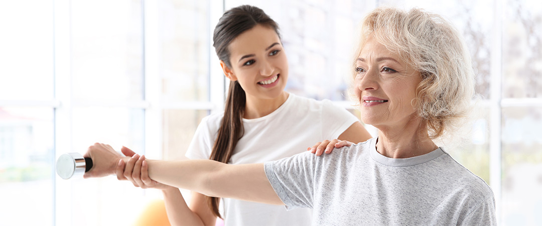 Physical therapist holding a resident's shoulder and wrist assisting with weights